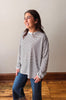 Woman wearing a striped long-sleeve shirt and jeans standing on a wooden floor.