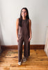 A woman modeling a brown sleeveless top and matching wide-leg pants set, standing on a wooden floor against a plain white wall.