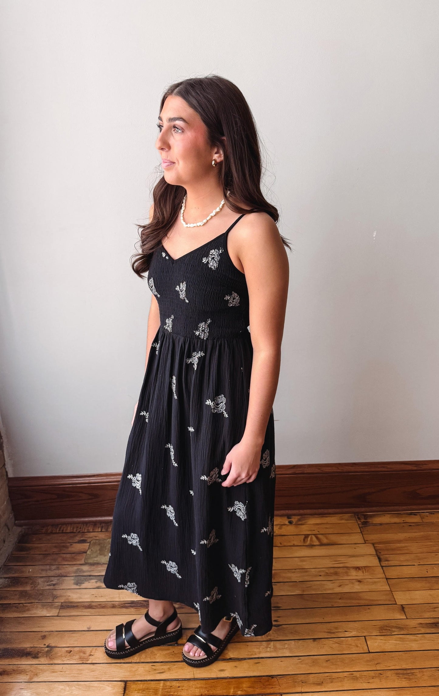 Woman wearing a black dress with white patterns on a wooden floor.