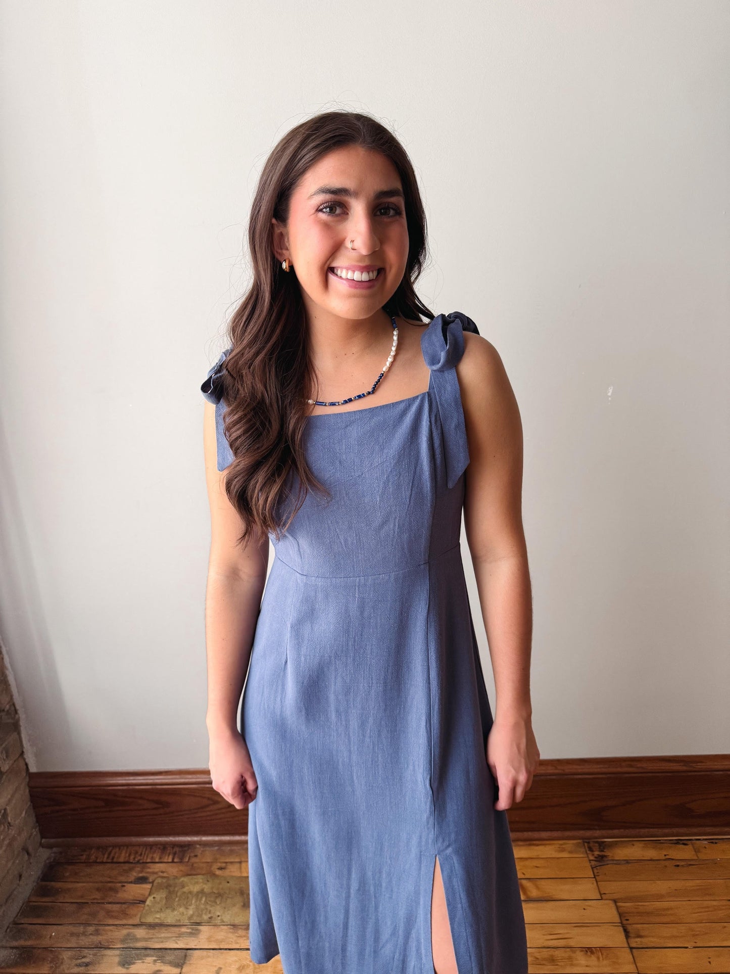 Woman wearing a blue dress standing against a white wall.