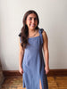 Woman wearing a blue dress standing against a white wall.