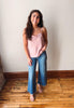 Woman wearing a pink top and blue jeans standing on a wooden floor against a white wall.