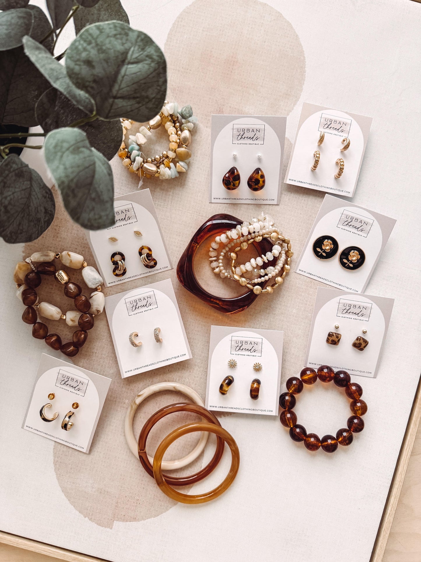 Collection of jewelry including bracelets and earrings on a light surface with greenery.