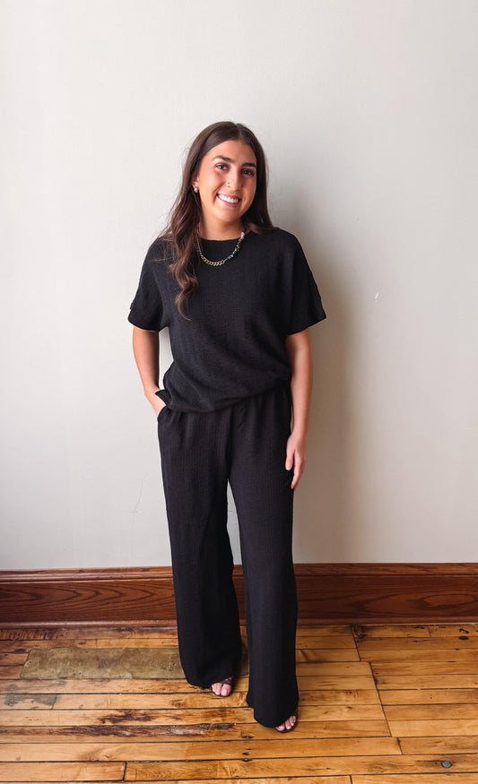 Woman wearing a black outfit standing against a plain wall.