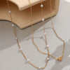 Gold necklace with heart charm and pearls on a light gray surface