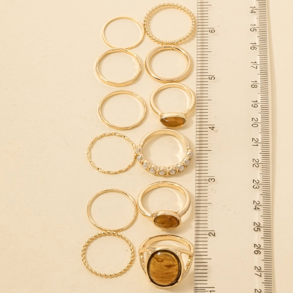 A set of gold rings displayed vertically next to a centimeter ruler on a light beige background, showing the size variation of the rings.