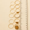 A set of gold rings displayed vertically next to a centimeter ruler on a light beige background, showing the size variation of the rings.