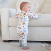 Baby in a onesie with animal prints standing in a living room.
