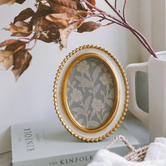 Decorative oval frame with floral design on a surface with books and a vase.