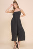 Woman wearing a black jumpsuit against a beige background