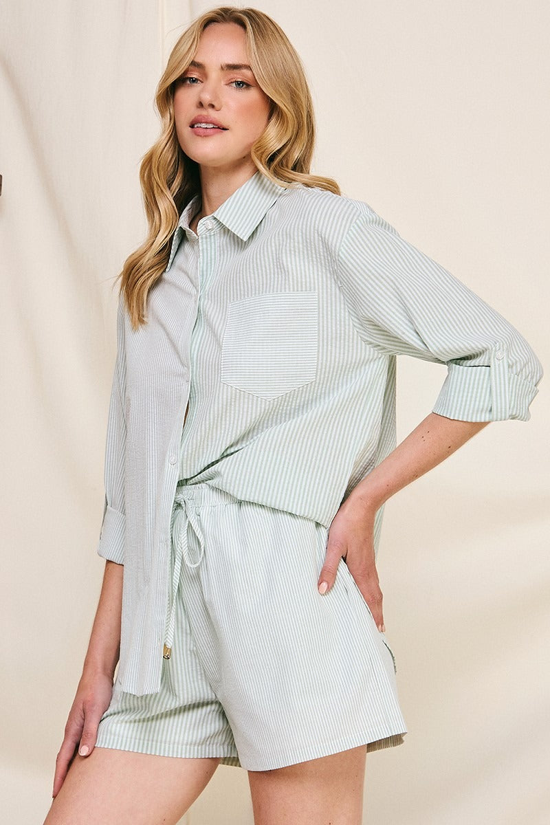 Woman wearing a light green striped shirt and shorts on a beige background