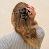 Person with long hair wearing black hair clips against a beige background