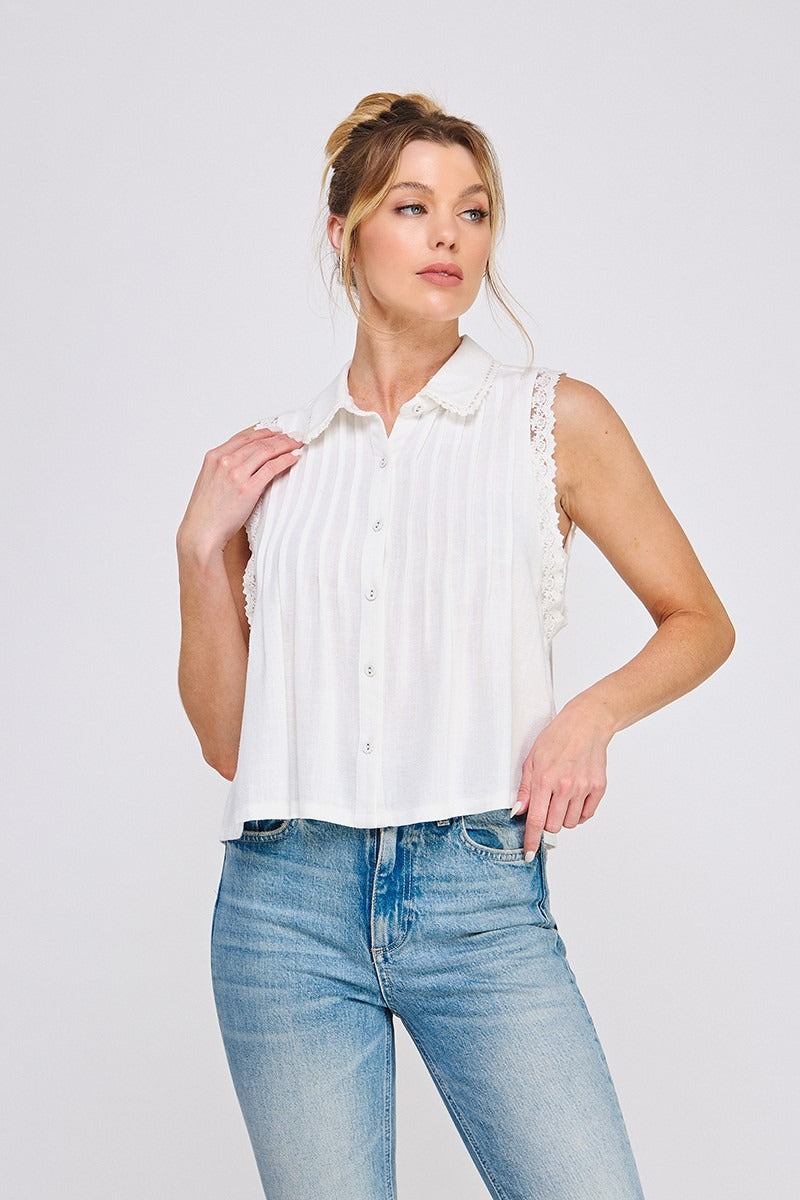 Woman wearing a white sleeveless blouse with ruffled collar and blue jeans on a light gray background