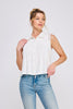 Woman wearing a white sleeveless blouse with ruffled collar and blue jeans on a light gray background