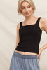 Woman wearing a black tank top and blue jeans against a beige background