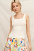 Woman wearing a white tank top and colorful patterned pants against a plain background