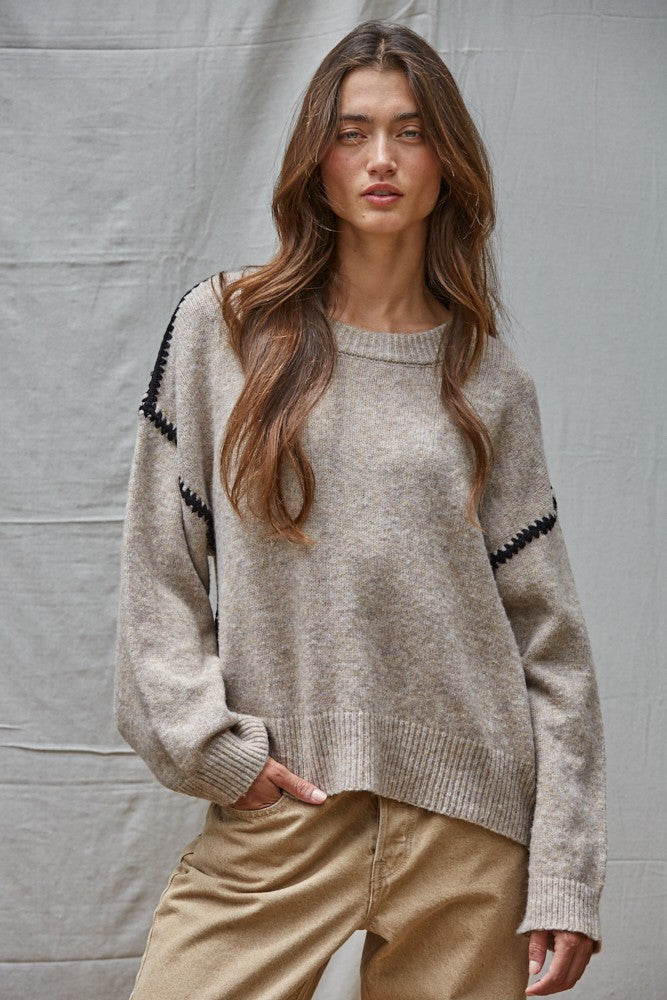 Woman wearing a beige sweater with black accents against a gray background