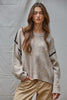 Woman wearing a beige sweater with black accents against a gray background