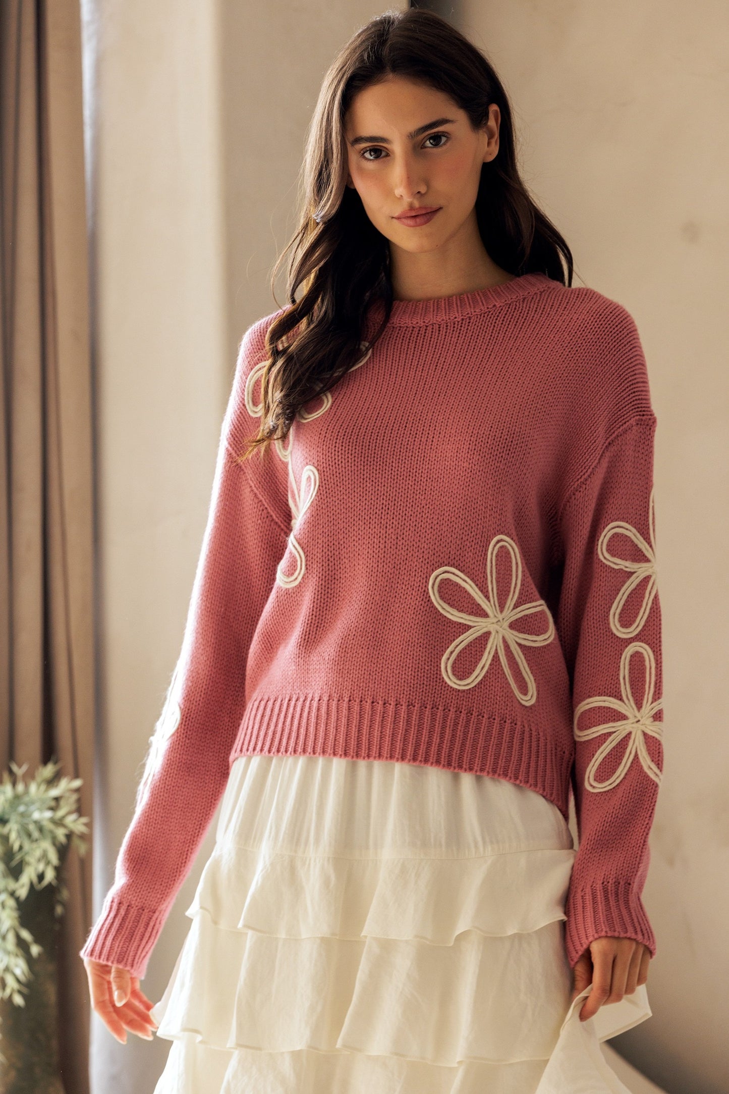 Woman wearing a pink sweater with floral designs in a neutral setting