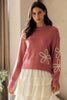 Woman wearing a pink sweater with floral designs in a neutral setting