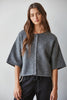 A woman wearing a cropped, short-sleeved gray knit cardigan with a button front, photographed against a plain light gray studio background.