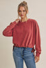 A woman wearing a dusty rose velvet long-sleeve sweatshirt with side ties and blue jeans, posing against a solid beige studio background.