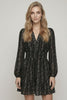 A woman modeling a black long-sleeve mini dress with a delicate white floral pattern, set against a plain light gray studio background.