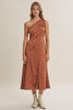 A woman modeling a rust-brown one-shoulder midi dress with white polka dots, paired with beige ankle boots, against a solid light beige studio background.