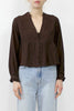 A woman wearing a dark brown long-sleeve blouse with a lace-up front and eyelet embroidery on the chest, paired with light-wash blue jeans, against a plain white background.