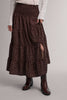 A dark brown smocked midi skirt with a small white floral pattern, featuring a side slit and pockets, styled with a cream knit top and dark brown ankle boots.