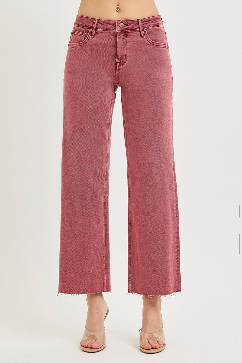 A model is wearing a pair of wide-leg cropped jeans in a dusty rose pink color, paired with clear high-heeled sandals, shown against a plain white studio background.