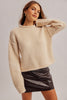 A woman wearing a cream-colored ribbed knit cropped sweater and a black faux-leather mini skirt, posing against a light gray studio background.
