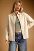 A woman modeling a light beige button-up overshirt over a black and white striped crop top with blue jeans, set against a solid warm brown studio background.