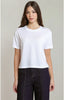 A woman modeling a white short-sleeve crewneck crop top paired with dark charcoal gray pants, set against a plain light gray studio background.