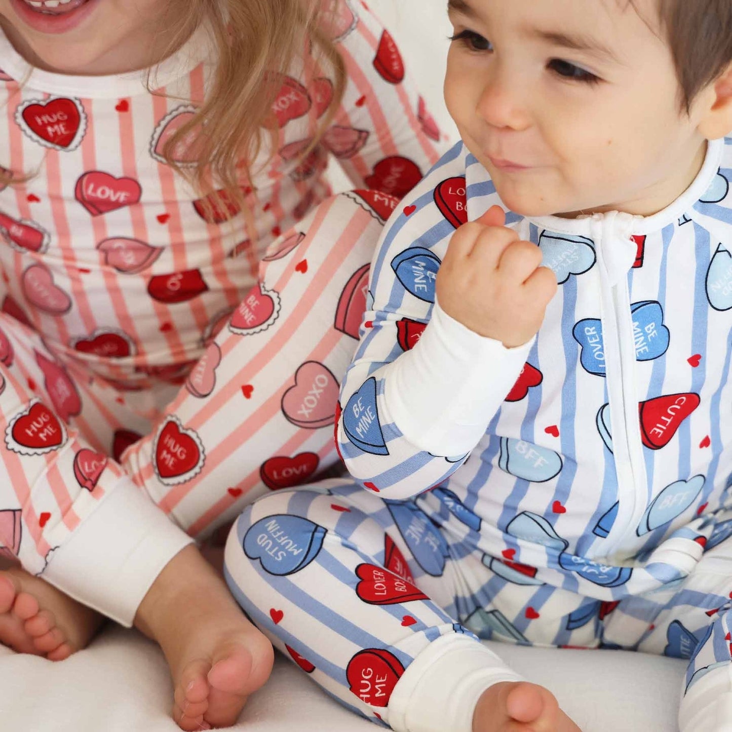 Two children wearing pajamas with heart patterns, one in pink and white and the other in blue and white.