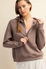 Woman wearing a brown zip-up hoodie against a beige background