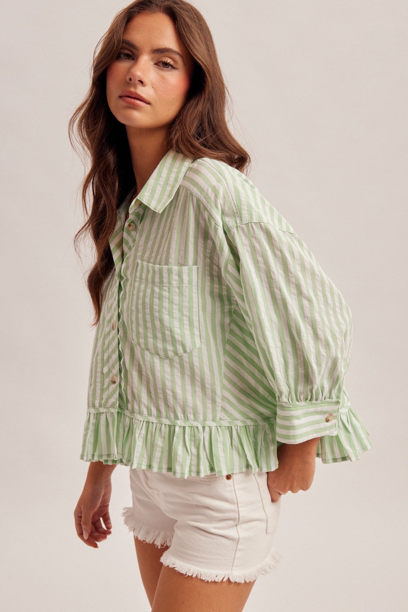 Woman wearing a green and white striped shirt with ruffled details on a plain background