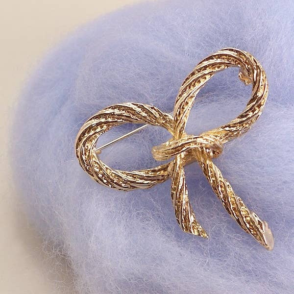 Gold bow-shaped brooch on a soft purple fabric background