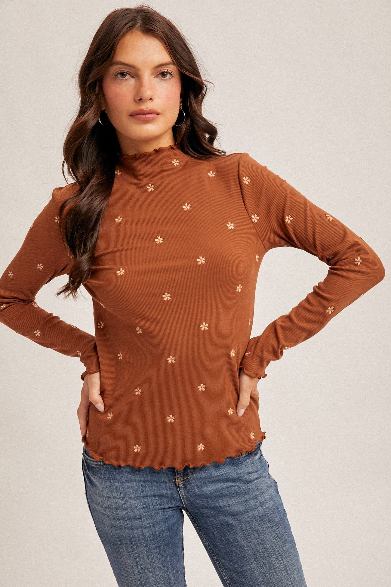 Woman wearing a brown long-sleeve top with floral patterns and blue jeans on a beige background