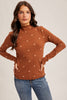 Woman wearing a brown long-sleeve top with floral patterns and blue jeans on a beige background