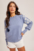 Woman wearing a blue sweater with white floral patterns on a plain background