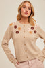 Woman wearing a taupe sweater with floral patterns on a plain background