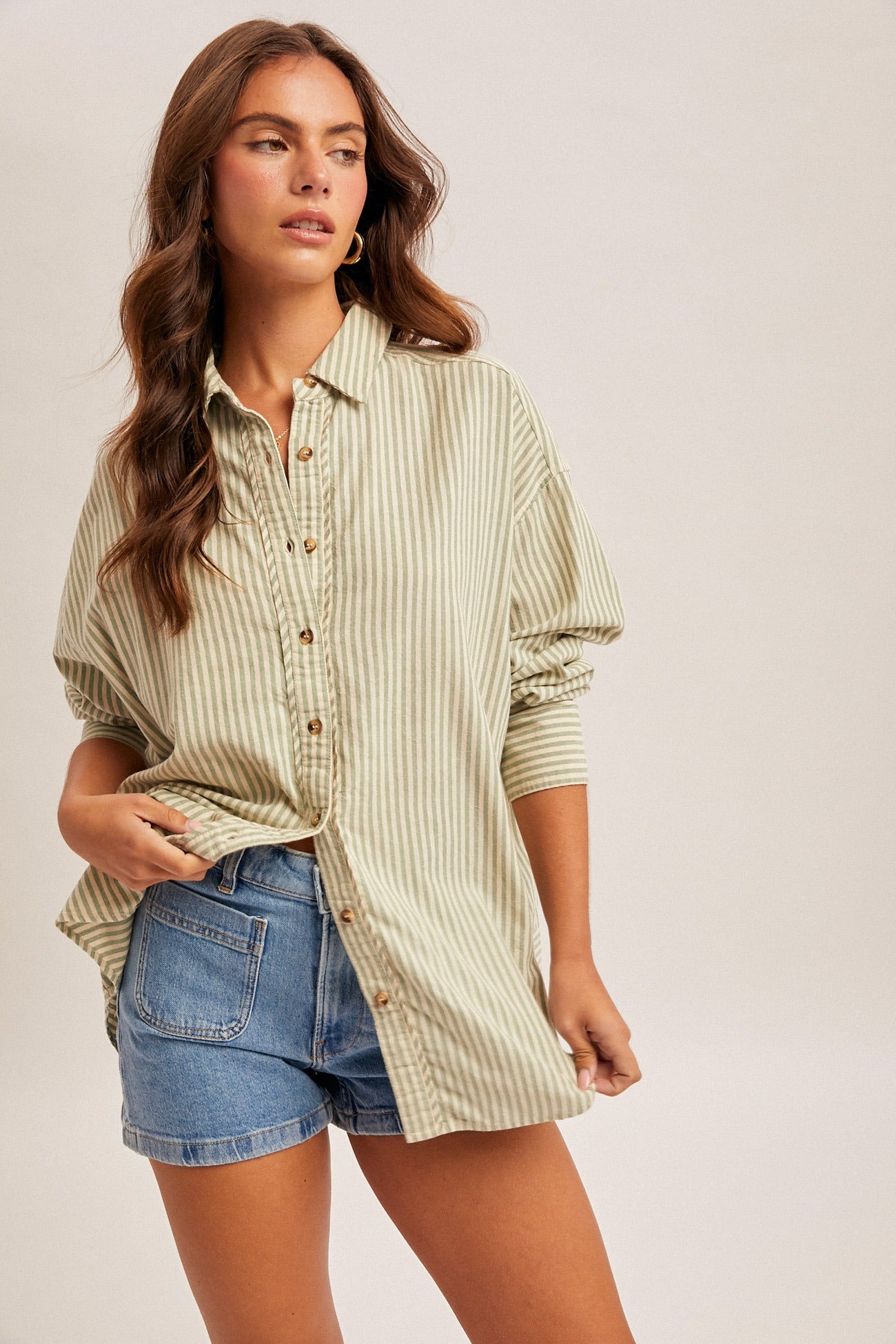 Woman wearing a striped shirt and denim shorts on a plain background