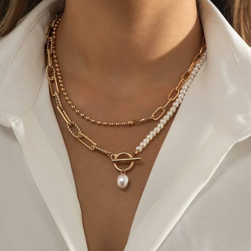 Close-up of a person wearing a gold chain necklace with a pearl pendant on a white shirt.