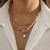 Close-up of a person wearing a gold chain necklace with a pearl pendant on a white shirt.