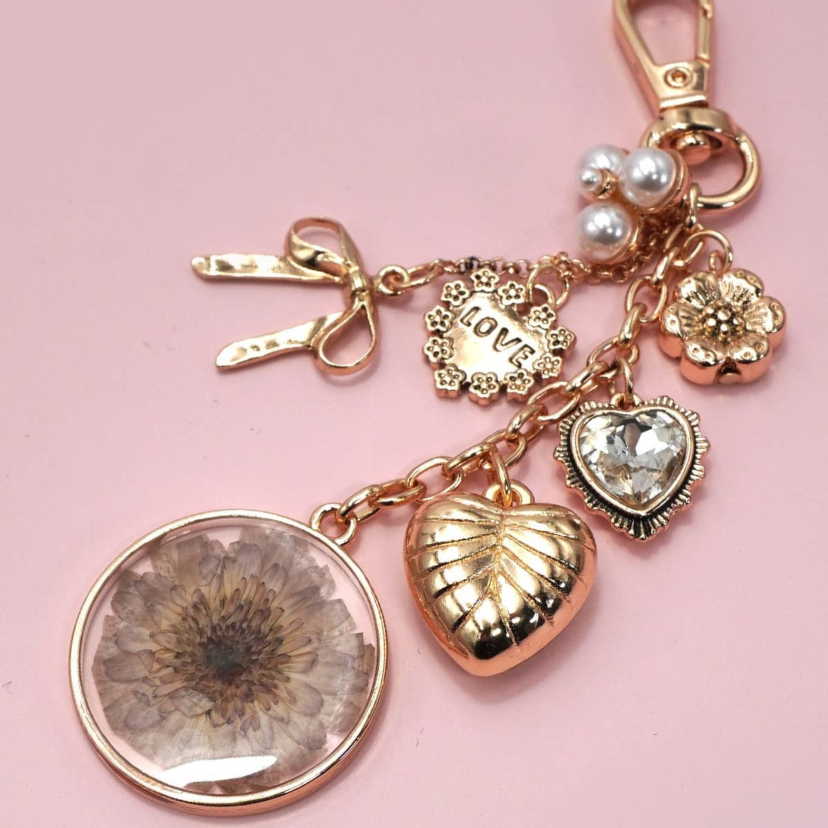 Gold keychain with floral and heart charms on a pink background