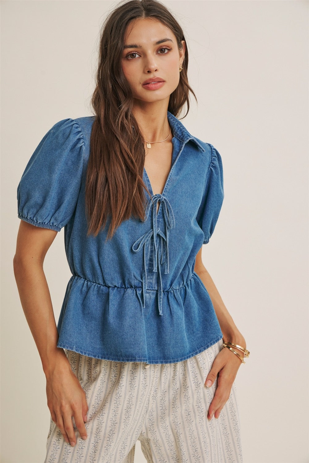 Woman wearing a blue denim top with puff sleeves on a beige background