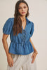 Woman wearing a blue denim top with puff sleeves on a beige background