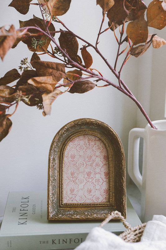 Decorative gold frame with floral pattern on a surface with books and a vase.