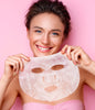 Woman holding a face mask against a pink background
